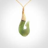 This picture shows a green jade hook pendant, also called a hei-matau, carved for us in New Zealand jade. The carver is Ric Moor - and this is a beautiful example of his work. The cord is a four-plait, adjustable fine beige coloured necklace.