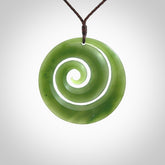 This picture shows a hand carved jade koru pendant. It is a darker green colour which is quite translucent where the jade is thin. The cord is hand plaited and adjustable so that you can position the pendant where it suits you best.