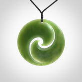 This picture shows a large hand carved jade koru pendant. It is a darker green colour which is quite translucent where the jade is thin. Although a large piece, it is a wonderful, delicate piece of jewellery. The cord is hand plaited and adjustable so that you can position the pendant where it suits you best.