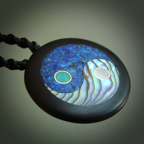 This photo shows a medium sized yin and yang pendant hand carved from horn with Mother of Pearl, Lapis Lazuli and Paua Shell inlay and brass. This is a stand out one off necklace for those who appreciate art to wear. It is provided with a cord in black that is a fixed length with Paua Shell Toggle. We ship this piece worldwide and shipping is included in the price.