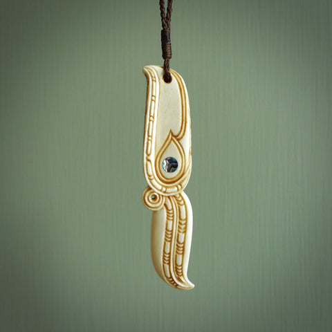 This picture shows a carved hawk in bone. It is a drop shaped pendant. The artist has carved traditional decorative kowhaiwhai designs into the body and these run up the sides of the hawk. These have specific meanings. It is provided with a hand-plaited brown cord that is length adjustable. Shipping is included and we ship worldwide.