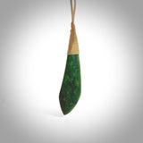 This photo shows a beautiful large jade drop. It is handcarved from a piece of green New Zealand pounamu, with fascinating light green inclusions throughout the stone. We have this on a creme coloured, adjustable four plait cord. We ship this worldwide with an express courier service. Postage is free.