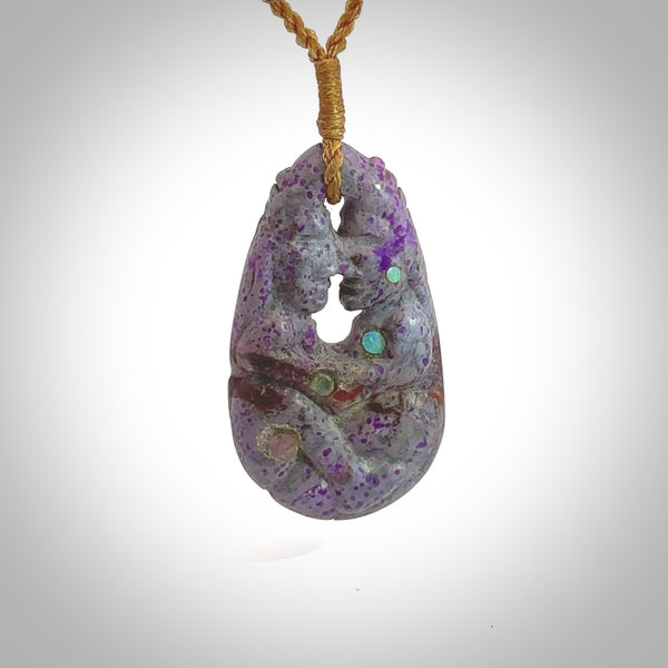 A large and beautiful hand carved partner hoongi pendant in sugilite. This piece is carved from purple Sugilite stone by Jeromy Van Riel with opal and rubys. This is a wonderful work of art to wear and comes with a hand-plaited cord and a bone toggle. A beautiful, unique pendant by Jeromy Van Riel for sale online.