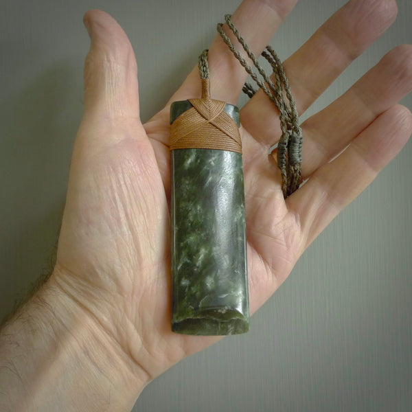 A large and beautiful hand carved toki pendant. This piece is carved from New Zealand jade by NZ Pacific. This is a wonderful large toki bound with a four-plaited khaki green cord and a Gingernut Brown lashing. A beautiful, traditional toki for sale online.