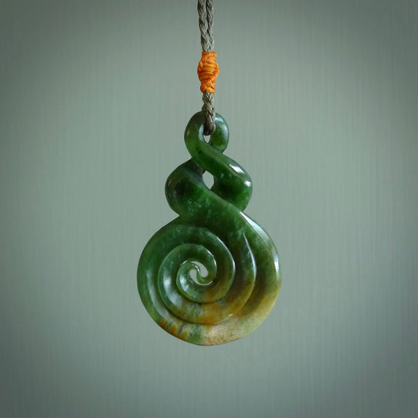 Ross Crump double twist with koru pendant. Hand carved from rare New Zealand jade this is a beautiful pounamu pendant. The cord is hand plaited in a brown colour and is length adjustable. It has a popper in burnt gold. It is a delicate and very beautiful greenstone pendant. For sale online by NZ Pacific.