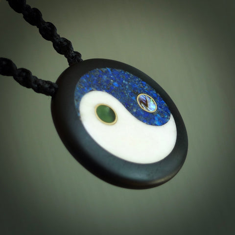 This photo shows a medium sized yin and yang pendant hand carved from horn with Bone, New Zealand Pounamu Jade, Lapis Lazuli and Paua Shell inlay alongside; brass. This is a stand out one off necklace for those who appreciate art to wear. It is provided with a cord in black that is a fixed length with Paua Shell Toggle. We ship this piece worldwide and shipping is included in the price.