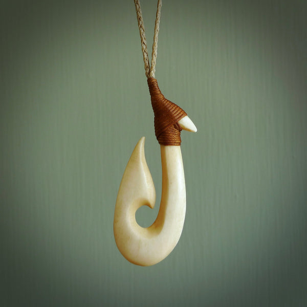 This is a larger engraved bone hook, or matau, pendant carved from a piece of bone. The cord is a Tan colour and the length of the cord can be adjusted. It is a large sized pendant and is well carved. A beautiful piece of traditional jewellery.
