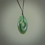 This picture shows a large hand-carved disc pendant. It is carved from British Columbian jade and is suspended from a hand-plaited, black cord. Free delivery worldwide. BC Jade contemporary necklace.