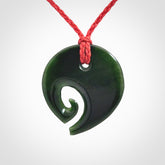 This photo shows a koru pendant carved from New Zealand Jade. We provide this piece with an adjustable red cord.