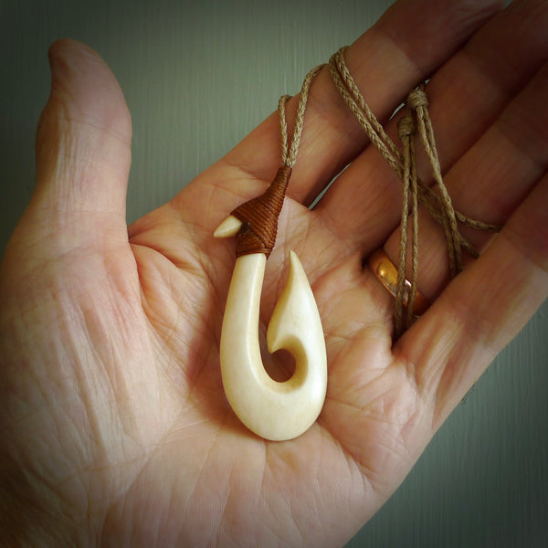 This is a larger engraved bone hook, or matau, pendant carved from a piece of bone. The cord is a Tan colour and the length of the cord can be adjusted. It is a large sized pendant and is well carved. A beautiful piece of traditional jewellery.