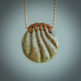This picture shows a hand carved sea shell disc pendant made from a flowering green/orange coloured flower jade. Hand made by Ana Krakosky. It is provided with an adjustable 4-Plait Kalahari tan cord and chestnut brown binding. Delivered to you with Express Courier.