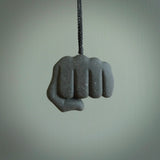 Greywacke Beach Stone fist bump, pendant hand made here in New Zealand. Hand carved by Rhys Hall for NZ Pacific. Handmade jewellery for sale online. The cord is black and has a loop and pebble toggle closure. Unique necklace for men and women. fist pump necklace hand made from New Zealand Greywacke Beach Stone.