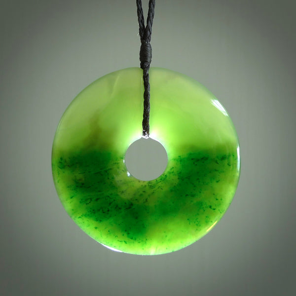 This picture shows a large hand-carved disc pendant. It is carved from British Columbian jade and is suspended from a hand-plaited, black cord. Free delivery worldwide. BC Jade contemporary necklace.