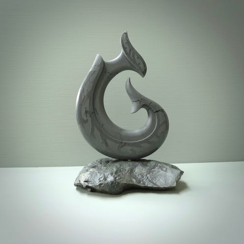Hand carved large New Zealand Argillite Stone Matau, hook carving displayed in a New Zealand Pākohe stand sculpture. Hand carved here in New Zealand by Kerry Thompson. This is a 'one only' sculpture, a beautiful display piece.