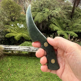 Hand holding a green knife with a forest background