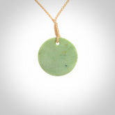 This piece is a small oval round, disc pendant carved in New Zealand Jade. It is suspended on a beige coloured braided cord that is length adjustable.
