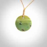 This piece is a small oval round, disc pendant carved in New Zealand Flower Jade. It is suspended on a beige coloured braided cord that is length adjustable.