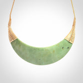 This picture shows a hand carved New Zealand jade contemporary half-shield pendant. It is a light green colour and is a wonderful, large piece of jewellery. The cord is hand plaited and adjustable so that you can position the pendant where it suits you best. This piece was carved for us by Donna Summers.