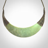 This picture shows a hand carved New Zealand flower jade contemporary half-shield pendant. It is a light green colour and is a wonderful, large piece of jewellery. The cord is hand plaited and adjustable so that you can position the pendant where it suits you best. This piece was carved for us by Donna Summers.