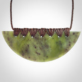 This picture shows a hand carved jade contemporary half-shield pendant. It is a semi-translucent green colour. The cord is hand plaited and adjustable so that you can position the pendant where it suits you best.