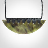 This picture shows a hand carved jade contemporary half-shield pendant. It is a semi-transluscent green colour. The cord is hand plaited and adjustable so that you can position the pendant where it suits you best.