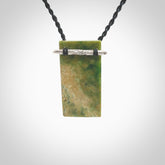 Hand carved New Zealand flower Jade rectangle drop with sterling silver rakau (talking stick) pendant. Made by Ana Krakosky for NZ Pacific in New Zealand Pounamu, jade. A beautiful orange and green marsden flower jade medium sized rectangle drop necklace with silver cast rakau, talking stick, provided on a black adjustable cord.