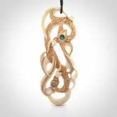 This picture shows a carved double manaia in bone. The artist has carved traditional decorative Koru designs into the face of the body and these run up the sides of the manaia head. These have specific meanings. It is provided with a hand-plaited brown cord that is length adjustable.