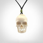 This picture shows a large sized Deer Antler Bone skull pendant that we have hand carved. It is polished to a soft shine and is a very striking piece. The cord is black and has a small green popper binding just above the pendant.
