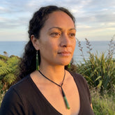 Woman with a necklace and matching earrings standing outdoors with plants and sky in the background