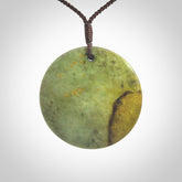 This piece is a large sized, oval round, disc pendant. It is suspended on a chocolate brown coloured braided cord that is length adjustable.