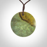 This piece is a large sized, oval round, disc pendant. It is suspended on a chocolate brown coloured braided cord that is length adjustable.