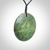 This piece is a large sized, oval round, disc pendant. It is suspended on a black coloured braided cord that is length adjustable.