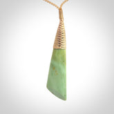 This photo shows a medium sized jade drop shaped pendant. It a a lovely varied green and light orange New Zealand Flower jade. The cord is a four plait beige and is adjustable in length.