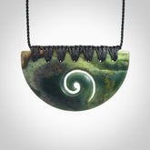 This picture shows a hand carved jade half-shield with Koru pendant. The cord is hand plaited and adjustable so that you can position the pendant where it suits you best.