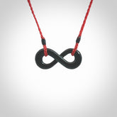 This piece is a fine, delicate eternity shaped pendant. It was carved from a lovely dark piece of black jade. It is suspended on an red braided cord that is length adjustable.