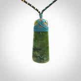 This photo shows a beautiful New Zealand jade toki suspended from a hand plaited adjustable cord. The binding around the top of the toki is a blue and bronze colour. The cord is length adjustable which allows the pendant to be positioned where it suits you best. The toki was carved for us by Jen Hung who is a wonderful jade carver from New Zealand.