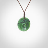 This pendant is a small sized and cupped koru necklace carved from a dark green piece of New Zealand Marsden Jade. Kyohei Noguchi carved this piece for us so the workmanship is outstanding. Handmade in New Zealand, a beautiful piece of jade jewellery. Provided with an adjustable brown cord and packaged in a woven kete pouch.