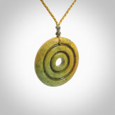 This picture shows a hand carved disc pendant made from a bright orange and green coloured flower jade. The front face is a unique design and the back is flat. It is provided with an adjustable sahara tan cord.