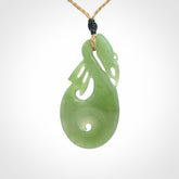 Hand carved New Zealand Inanga jade manaia with koru pendant. Carved from beautiful New Zealand Jade for NZ Pacific by Ross Crump. Unique jade jewellery for sale online. Provided with an adjustable tan cord.