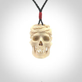 This picture shows a medium sized Deer Antler Bone pirate skull pendant that we have hand carved. The cord is a black colour and has a small red binding just above the pendant.