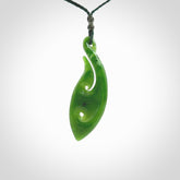 This photo shows a large matau, or hook, pendant carved in deep green New Zealand Jade. It is a very interesting piece which has a koru carved into the centre of the hook. It is strung on a manuka green cord which is adjustable. The artist who carved this pendant is Ross Crump, a master carver of jade from New Zealand.