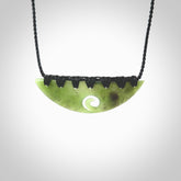This picture shows a hand carved jade half-shield with Koru pendant. It is a semi-translucent green colour. This is a wonderful piece of jewellery. The cord is hand plaited and adjustable so that you can position the pendant where it suits you best. This piece was carved for us by Ric Moor. Delivery is free worldwide.