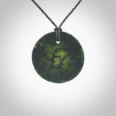 A lovely disc design with cupping on one side and the lightly convex form on the other - a little feature that captures the light and gives the piece a sense of movement and form. Hand made from New Zealand Jade by Ric Moor. Delivered with an adjustable black cord.