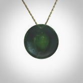 This piece is a oval round, cupped disc pendant. It was carved for us by Ric Moor from a lovely dark green piece of New Zealand jade. It is suspended on a khaki coloured braided cord that is length adjustable.
