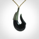 This photo shows a New Zealand Tangiwai hook, or matau, pendant. The plaited cord is khaki and the length can be adjusted.