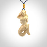 This photo shows a photo of a mermaid pendant. It is handcarved from a beautifully creamy piece of woolly mammoth tusk. It is suspended on an adjustable cord.