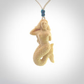 This photo shows a photo of a mermaid pendant. It is handcarved from a beautifully creamy piece of woolly mammoth tusk. It is suspended on an adjustable cord.