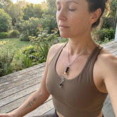 Woman in a brown tank top with a necklace, sitting outdoors on a wooden deck.