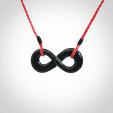 This piece is a fine, delicate eternity shaped pendant. It was carved from a lovely dark piece of black jade. It is suspended on an red plaited cord that is length adjustable.