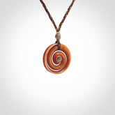 A hand carved and intricate koru pendant made for us by Yuri Terenyi. This is a beautiful little piece and is emblematic of the well known and loved Koru design. It is carved from stained bone in a hollowed, koru spiral shape with paua shell inlay in the middle of the koru. It is suspended from a gingernut brown/wapiti brown cord with a stardust floret and the necklace is adjustable.
